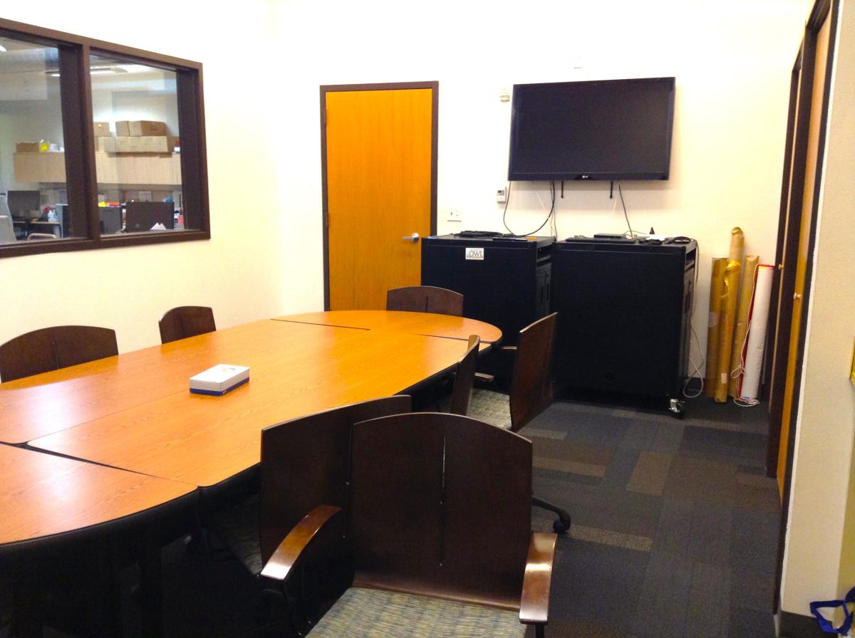 Shared Conference Room. Has a modular table setup, chairs, and a flat TV screen.